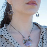 A necklace with a braided design featuring amethyst gemstones and a mix of natural gemstones, with a hammered brass and sterling silver twist. The pendant is accompanied by an oxidized sterling silver chain and a handmade clasp.