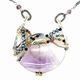 A necklace with a braided design featuring amethyst gemstones and a mix of natural gemstones, with a hammered brass and sterling silver twist. The pendant is accompanied by an oxidized sterling silver chain and a handmade clasp.