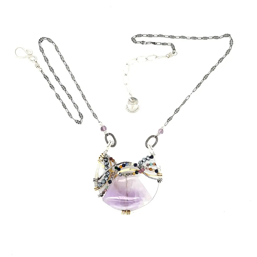 A necklace with a braided design featuring amethyst gemstones and a mix of natural gemstones, with a hammered brass and sterling silver twist. The pendant is accompanied by an oxidized sterling silver chain and a handmade clasp.