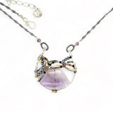 A necklace with a braided design featuring amethyst gemstones and a mix of natural gemstones, with a hammered brass and sterling silver twist. The pendant is accompanied by an oxidized sterling silver chain and a handmade clasp.