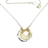 Sterling silver hammered circle pendant with brass circle inside holding a fresh water pearl surrounded by gold filled arches on a sterling silver textured chain