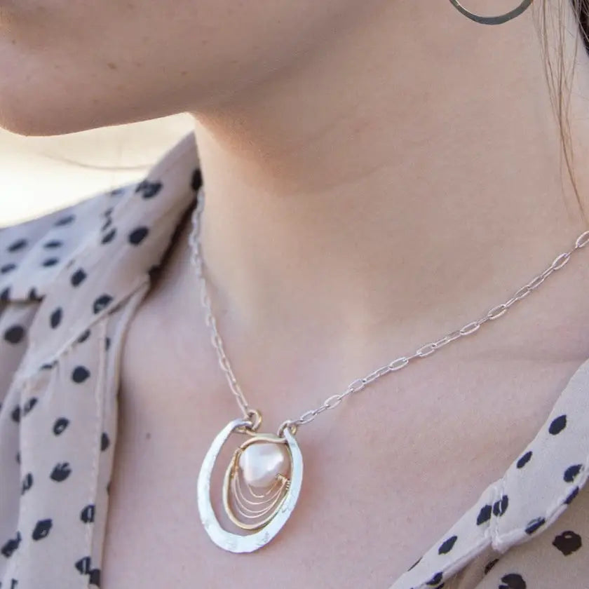 Sterling silver hammered circle pendant with brass circle inside holding a fresh water pearl surrounded by gold filled arches on a sterling silver textured chain