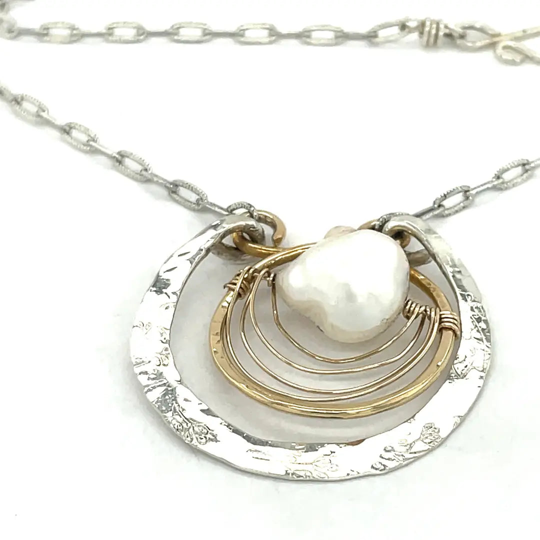 Sterling silver hammered circle pendant with brass circle inside holding a fresh water pearl surrounded by gold filled arches on a sterling silver textured chain