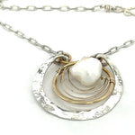 Sterling silver hammered circle pendant with brass circle inside holding a fresh water pearl surrounded by gold filled arches on a sterling silver textured chain