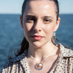 Sterling silver hammered circle pendant with brass circle inside holding a fresh water pearl surrounded by gold filled arches on a sterling silver textured chain