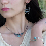 A darkened sterling silver crescent necklace  featuring a bright blue druzy quartz slab and ombre blue tourmaline gemstones on gold filled wire