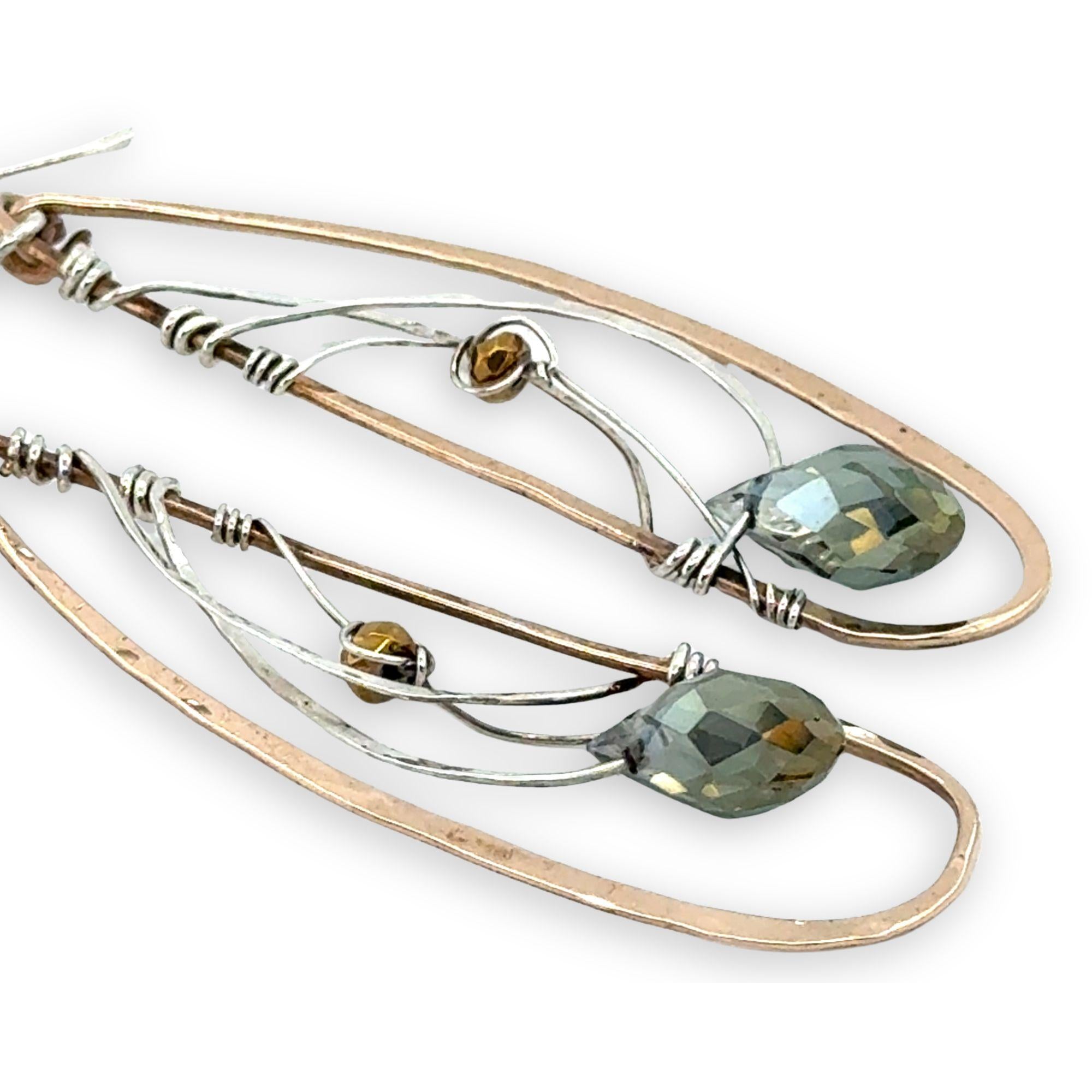 Handmade hammered bronze wings are embellished with sterling silver weaving holding a blue green crystal drop 