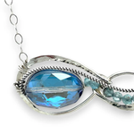 A sterling silver infinity pendant necklace with a twisted silver ring and an adjustable delicate chain. The pendant features apatite faceted gemstone accenting blue crystal.
