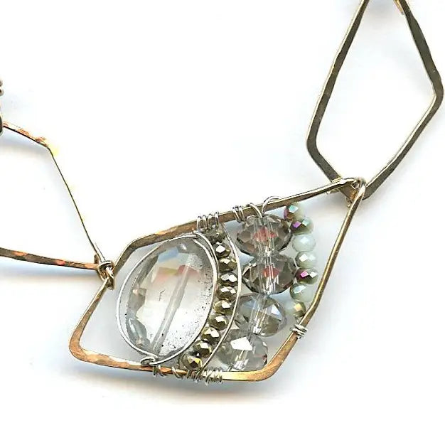 A faceted clear quartz oval gemstone is layered with pyrite and crystals on sterling silver wire inside a bronze parallelogram, then attached to three varying sized parallelograms