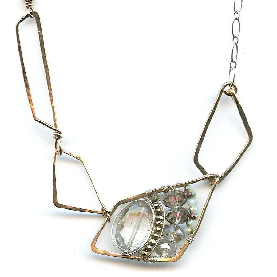 A faceted clear quartz oval gemstone is layered with pyrite and crystals on sterling silver wire inside a bronze parallelogram, then attached to three varying sized parallelograms