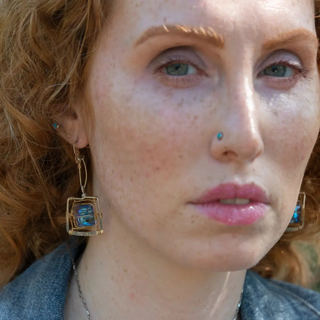 Faceted blue crystal tiles are wrapped tightly in brass twist wire inside a stamped sterling silver box earring, hanging from a gold filled link
