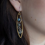 A pair of handmade brass twisted marquise earrings with hammered sterling silver and sparkling crystals in blue, green, and grey colors.