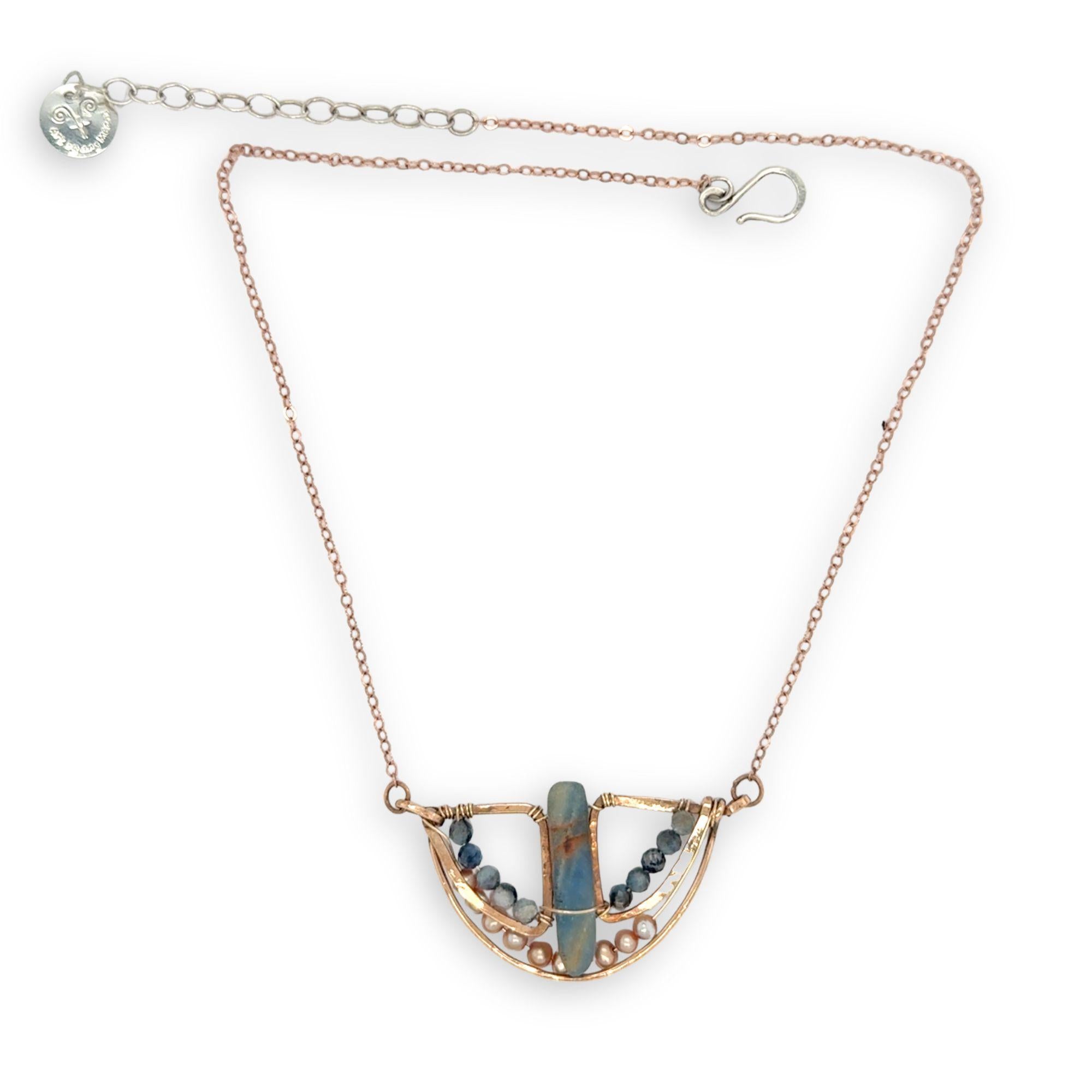 Aquamarine smooth slab is held in the center of a bronze semi circle necklace that's lined with champagne fresh water pearl and aquamarine faceted gemstones on rose gold chain necklace