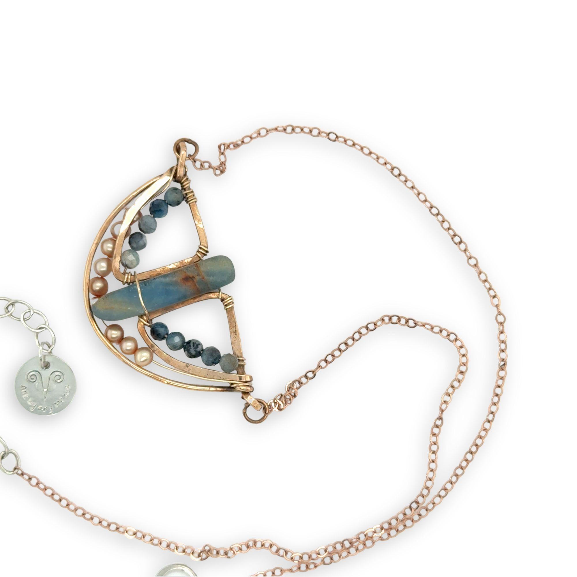 Aquamarine smooth slab is held in the center of a bronze semi circle necklace that's lined with champagne fresh water pearl and aquamarine faceted gemstones on rose gold chain necklace
