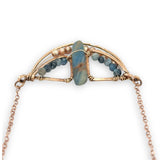Aquamarine smooth slab is held in the center of a bronze semi circle necklace that's lined with champagne fresh water pearl and aquamarine faceted gemstones on rose gold chain necklace