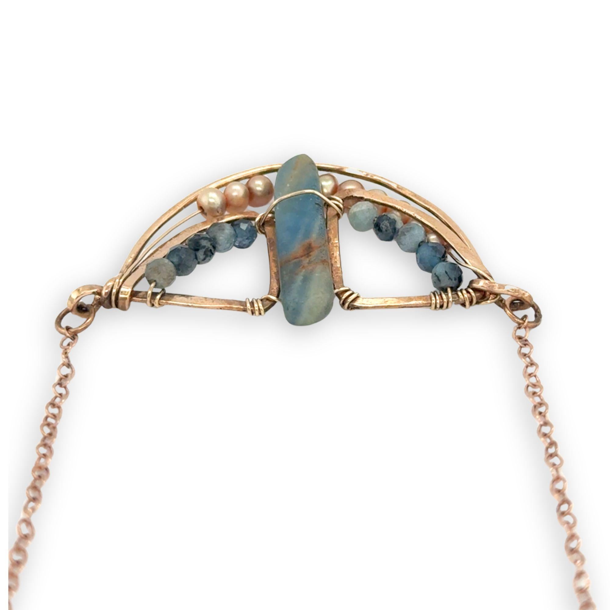 Aquamarine smooth slab is held in the center of a bronze semi circle necklace that's lined with champagne fresh water pearl and aquamarine faceted gemstones on rose gold chain necklace