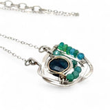 A sterling silver necklace with a faceted dark teal apatite coin set in gold fill centers, surrounded by cubic zirconia and green opal gemstones, with a mini sterling silver clasp.