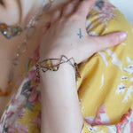 A handcrafted cuff bracelet featuring a mix of yellow opal, faceted citrine, banded agate, and hessonite raw crystal, wrapped in gold fill and set in among brass and oxidized sterling silver geometric cuff bracelet that's been stamped with trees