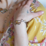 A handcrafted cuff bracelet featuring a mix of yellow opal, faceted citrine, banded agate, and hessonite raw crystal, wrapped in gold fill and set in among brass and oxidized sterling silver geometric cuff bracelet that's been stamped with trees