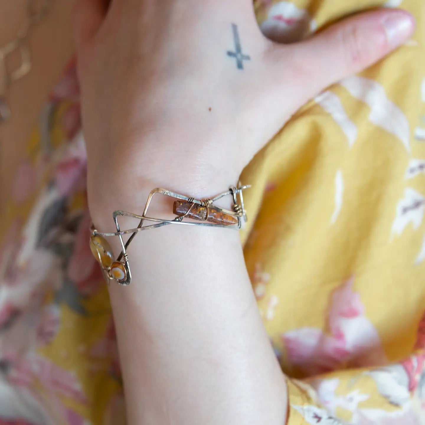 A handcrafted cuff bracelet featuring a mix of yellow opal, faceted citrine, banded agate, and hessonite raw crystal, wrapped in gold fill and set in among brass and oxidized sterling silver geometric cuff bracelet that's been stamped with trees