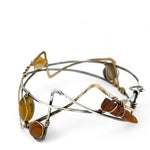 A handcrafted cuff bracelet featuring a mix of yellow opal, faceted citrine, banded agate, and hessonite raw crystal, wrapped in gold fill and set in among brass and oxidized sterling silver geometric cuff bracelet that's been stamped with trees