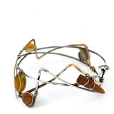 A handcrafted cuff bracelet featuring a mix of yellow opal, faceted citrine, banded agate, and hessonite raw crystal, wrapped in gold fill and set in among brass and oxidized sterling silver geometric cuff bracelet that's been stamped with trees
