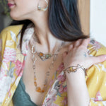 A handcrafted cuff bracelet featuring a mix of yellow opal, faceted citrine, banded agate, and hessonite raw crystal, wrapped in gold fill and set in among brass and oxidized sterling silver geometric cuff bracelet that's been stamped with trees