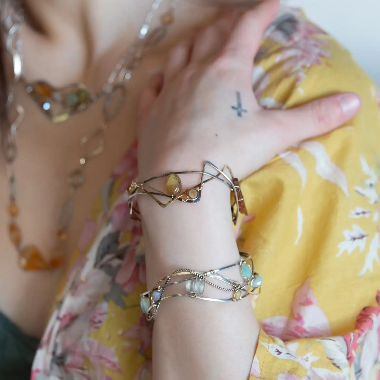A handcrafted cuff bracelet featuring a mix of yellow opal, faceted citrine, banded agate, and hessonite raw crystal, wrapped in gold fill and set in among brass and oxidized sterling silver geometric cuff bracelet that's been stamped with trees