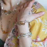 A handcrafted cuff bracelet featuring a mix of yellow opal, faceted citrine, banded agate, and hessonite raw crystal, wrapped in gold fill and set in among brass and oxidized sterling silver geometric cuff bracelet that's been stamped with trees