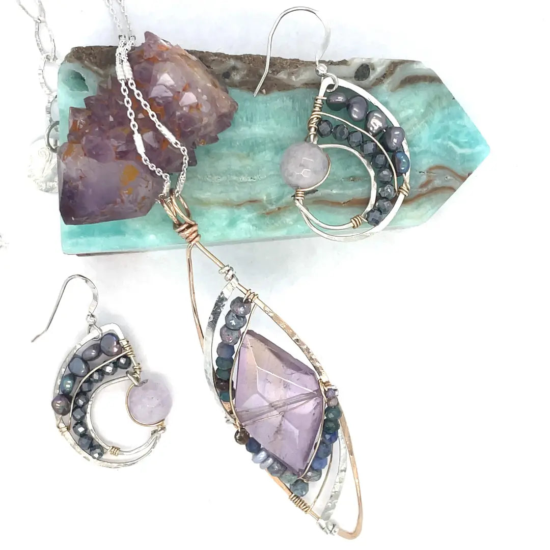 A necklace with a bronze marquise pendant featuring a ametyst center stone encrusted with ruby zoisite, fresh water pearl, and sodalite gemstones with sterling silver wire accent