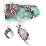 A necklace with a bronze marquise pendant featuring a ametyst center stone encrusted with ruby zoisite, fresh water pearl, and sodalite gemstones with sterling silver wire accent