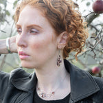 Woman with red hair and garnet earrings standing in front of an apple tree