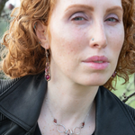 Close-up of a person with red hair wearing earrings and a necklace outdoors.