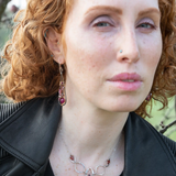 Close-up of a person with red hair wearing earrings and a necklace outdoors.