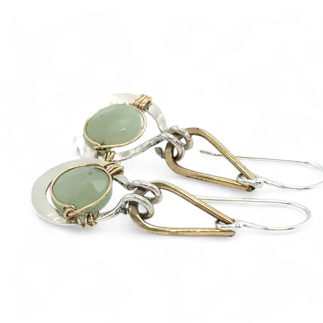 Pair of earrings with green jade gemstones and gold and silver hooks on a white background