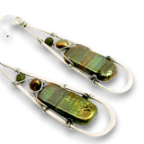 A pair of long teardrop-shaped earrings made from silver wire frames, featuring large baroque-style green iridescent beads and small dark green and brown beads, shown on a white background.