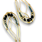 A pair of gold-toned statement earrings with abstract, flowing wireframe loops accented by faceted beads in black, olive green, and iridescent blue-green.