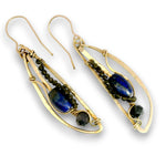 A pair of gold dangle earrings with dark blue lapis lazuli stones, small dark green beads, and faceted black beads, shown on a white background.