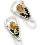A pair of handmade dangle earrings featuring a large smooth brown stone, small iridescent beads, and silver wire wrapping with fishhook backings, shown on a white background.