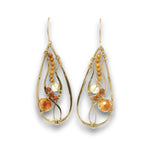 A pair of gold teardrop dangle earrings with small amber-orange beads, a faceted clear crystal, and a larger round amber-orange stone, shown on a white background.