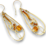 A pair of gold teardrop dangle earrings with wire-wrapped details, featuring round amber-orange and clear faceted gemstones, shown on a white background.