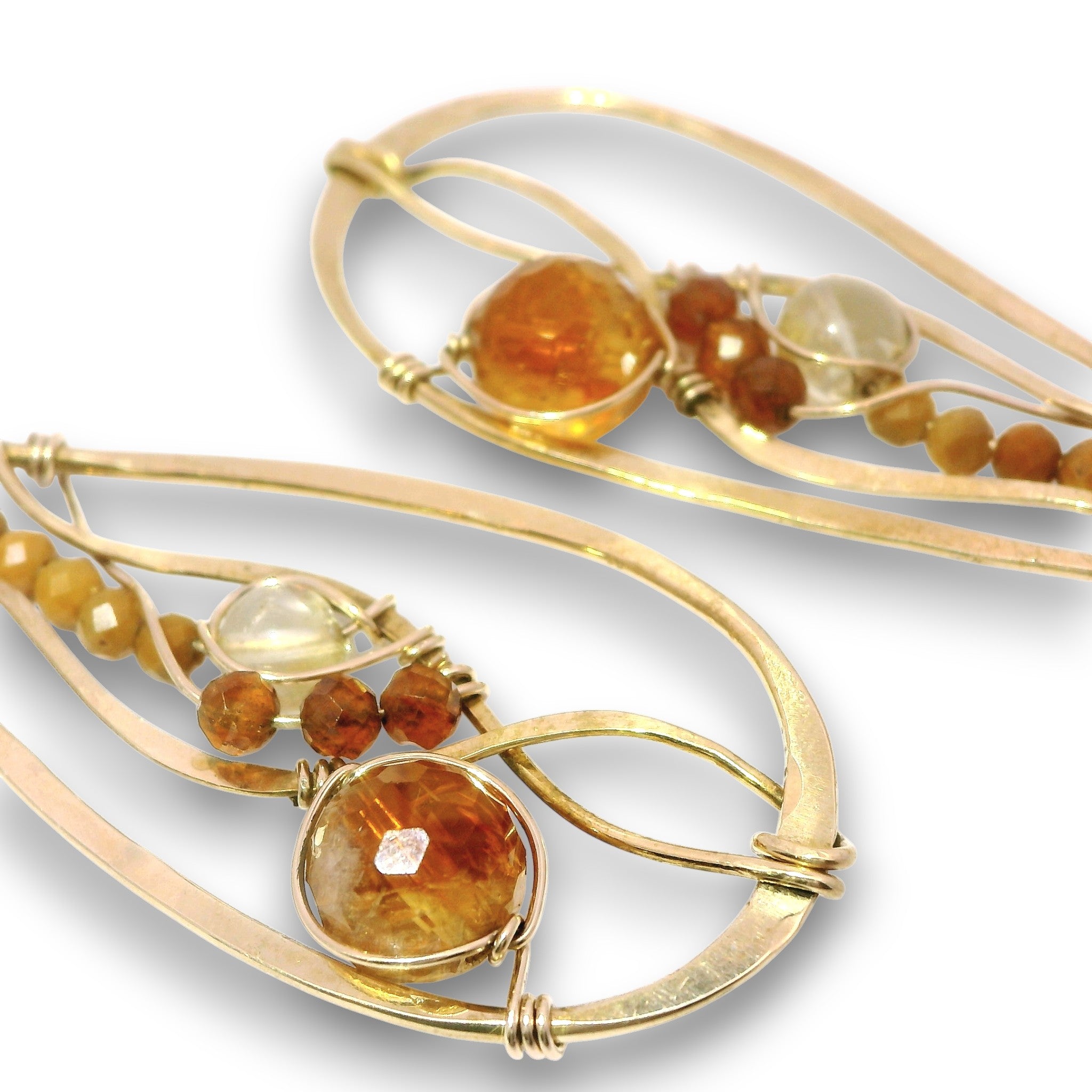 A pair of gold-toned statement earrings with organic, flowing wire designs, featuring round and faceted amber-orange and clear gemstones on a white background.