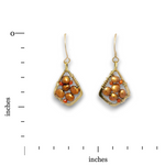 A pair of gold-toned drop earrings with clustered brown and orange faux pearl beads, shown on a white background with a vertical inch ruler on the left and an inch scale at the bottom for size reference.