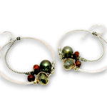 A pair of handmade silver hoop earrings with twisted wire details, featuring green and dark red beads, set against a plain white background.