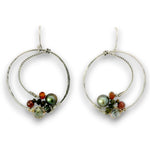 A pair of silver hoop earrings with textured and twisted wire details, decorated with green and black pearls, small orange beads, and clear faceted beads on a white background.