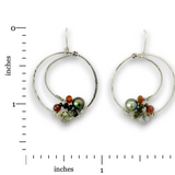 A pair of silver hoop earrings with small gemstone clusters, shown on a white background with inch measurement markers. The earrings feature textured and twisted silver hoops with a cluster of beads at the bottom, including a dark green freshwater pearl, orange and black beads, and a light green stone.