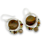 A pair of handmade dangle earrings featuring large polished brown tiger's eye stones in silver hoops, accented with small green and brown beads, on a white background.