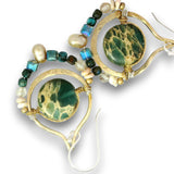A pair of gold hoop earrings featuring round green marbled stone centers, accented with small faceted beads in teal, blue, brown, and cream on a white background.