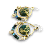 A pair of handmade dangle earrings featuring round green and black marbled stone centers, gold-tone crescent-shaped wire frames, and beaded strands with pearls, beads, and iridescent accents, shown on a white background.