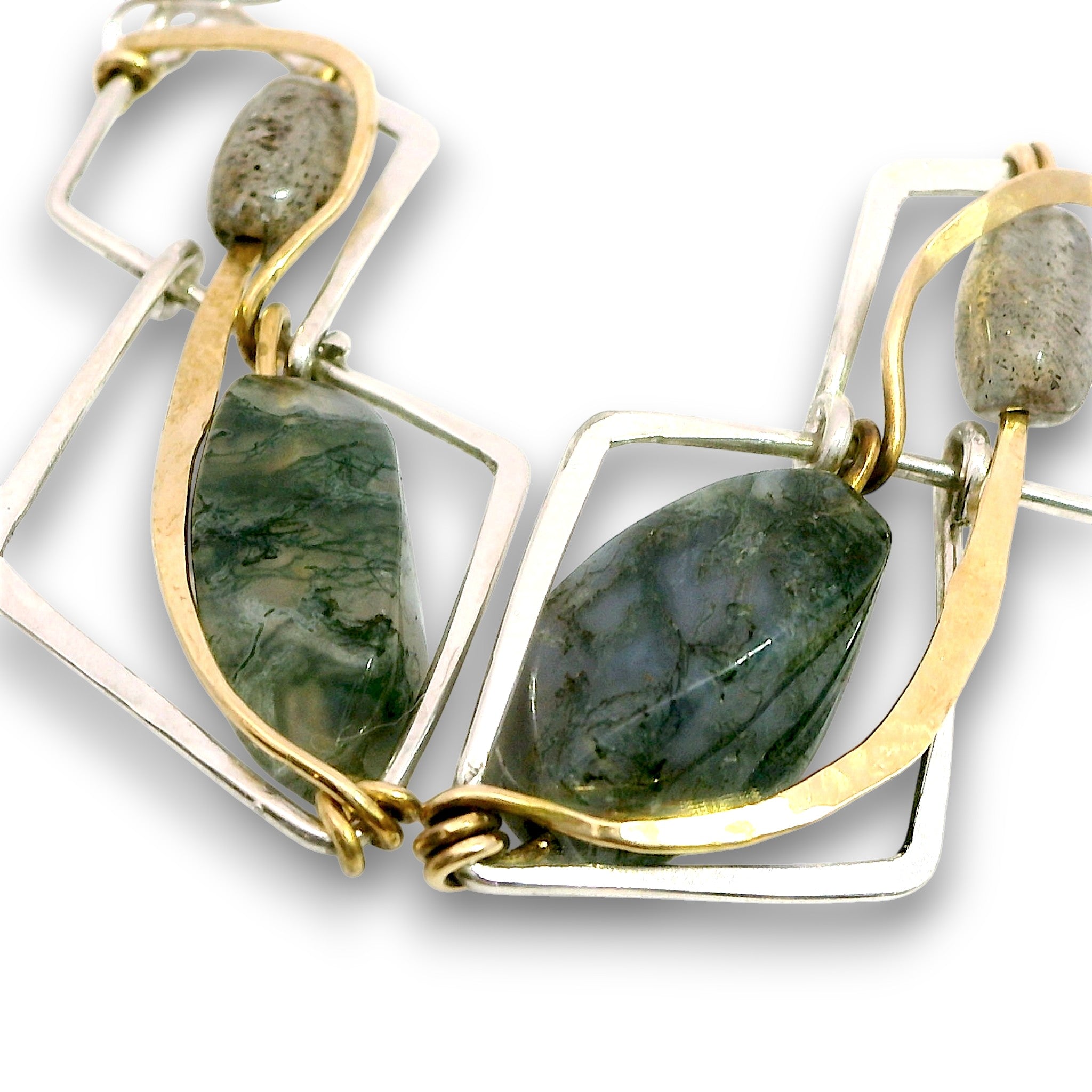 A close-up of a geometric statement necklace featuring polished green stone pendants, gold-toned curved wire, and silver-toned rectangular frames on a white background.
